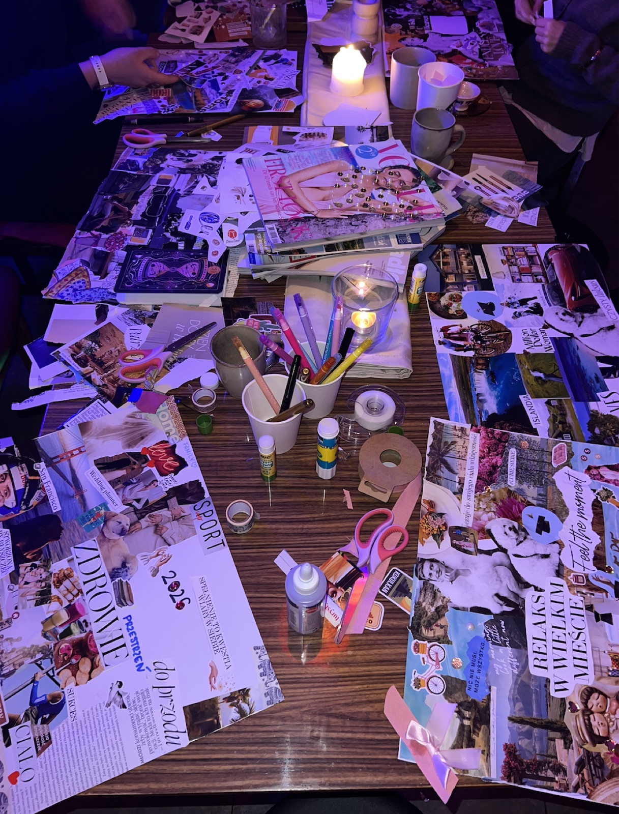 Stół podczas warsztatów tworzenia vision board - wycinanki z magazynów, świeczki tworzące nastrojowe oświetlenie, uczestnicy warsztatów przy wspólnym stole.